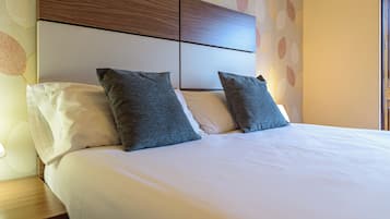Una cama bien hecha con ropa de cama blanca y gris, un cabecero de madera y una pared con un diseño de hojas.