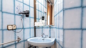 Casa de banho com uma pia branca, paredes azulejadas em azul, um secador de cabelo e um espelho.