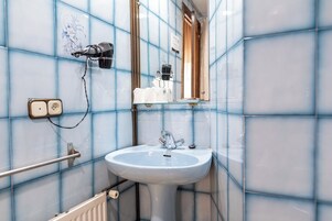 Un baño con lavamanos blanco, paredes de azulejos azules, secador de pelo y espejo.