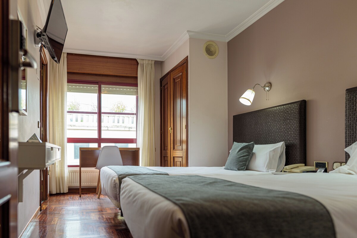 A hotel room with two beds, a desk, and a window with curtains.