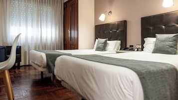 A hotel room with two beds, a desk, and a chair.