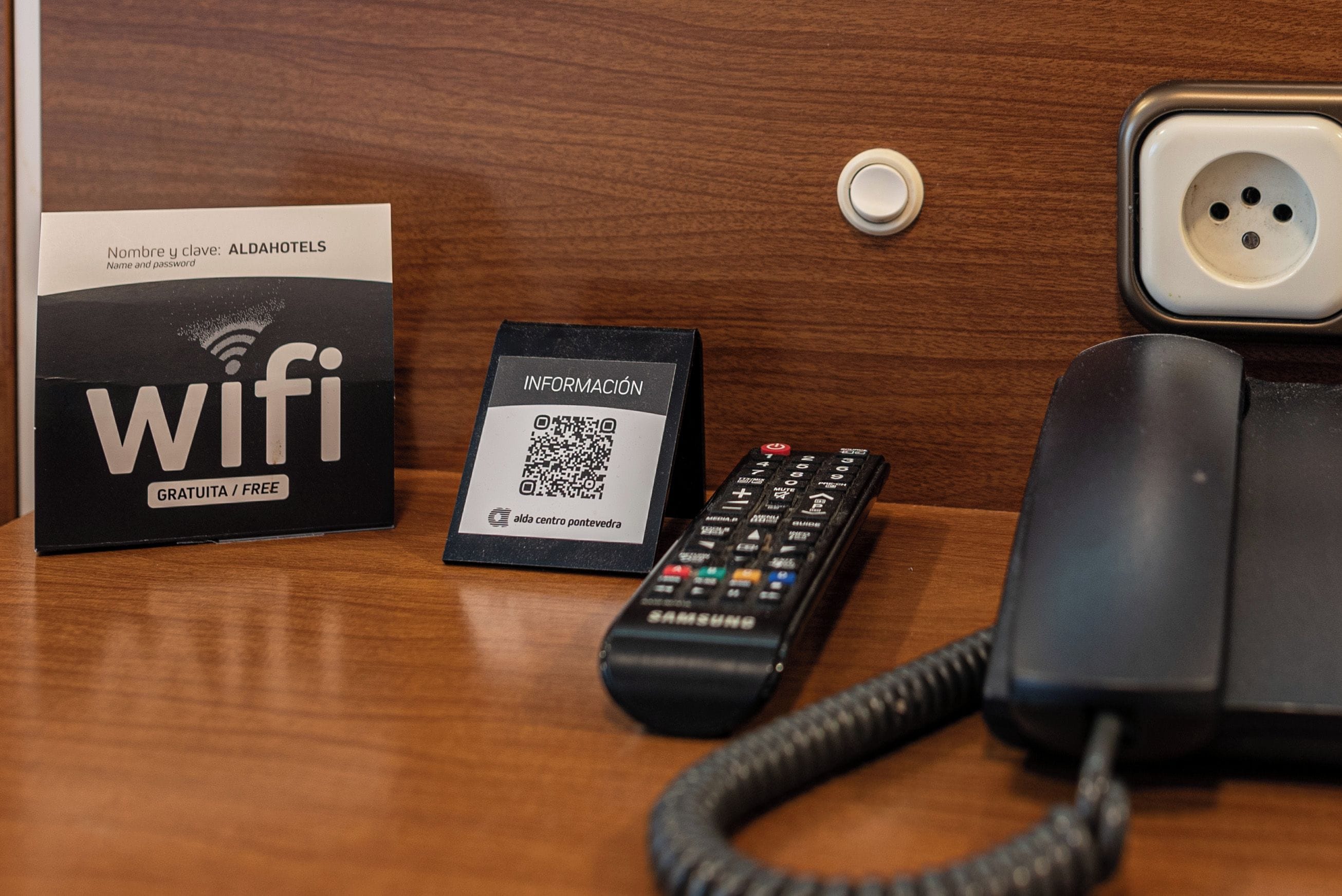 Ein Holztisch mit einer schwarzen Fernbedienung, einer weißen Karte mit einem QR-Code und einem schwarzen Telefon.