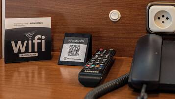 Ein Holztisch mit einer schwarzen Fernbedienung, einer weißen Karte mit einem QR-Code und einem schwarzen Telefon.