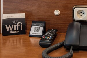 Una mesa de madera con un control remoto negro, una tarjeta blanca con un código QR y un teléfono negro.