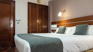 A hotel room with a large bed, wooden wardrobe, and a wall-mounted light fixture.