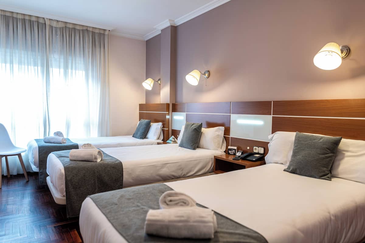 A hotel room with two beds, a desk, and a chair. There are two bedside tables with lamps and a phone.