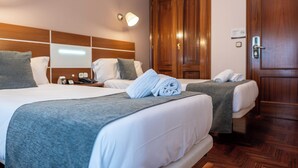 Quarto de hotel com duas camas, cabeceiras de madeira, um guarda-roupa de madeira e uma mesa de cabeceira com abajur.