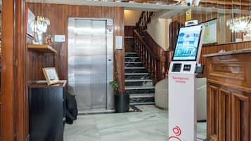Un área de recepción con mostrador, quiosco informativo digital, escalera y planta en maceta.