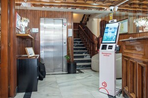 A reception area with a reception desk, a digital information kiosk, a staircase, and a potted plant.