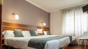 Quarto de hotel com duas camas, televisão, cadeira e janela com cortinas.