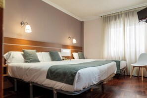 Ein Hotelzimmer mit zwei Betten, einem Fernseher, einem Sessel und einem Fenster mit Vorhängen.