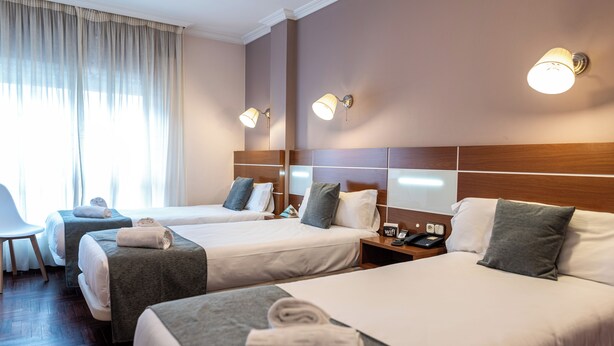 Quarto de hotel com duas camas, uma mesa e uma cadeira. Há duas mesas de cabeceira com luminárias e um telefone.