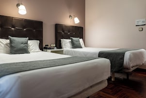 Habitación de hotel con dos camas, cada una con cabecero, ropa blanca y una manta gris. Hay lámparas de pared sobre cada cama.