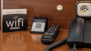 Ein Holztisch mit einer schwarzen Fernbedienung, einer weißen Karte mit einem QR-Code und einem schwarzen Telefon.