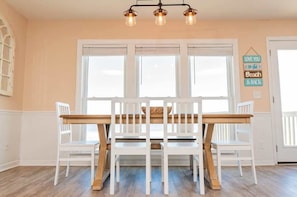 Un comedor con una mesa de madera y sillas blancas, una lámpara colgante y un letrero en la pared.