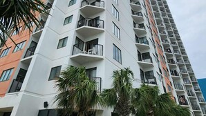 A high-rise residential building with multiple balconies, palm trees, and a clear sky. - Coastal Luxe | Palace Twenty Oh Eight (Myrtle Beach)