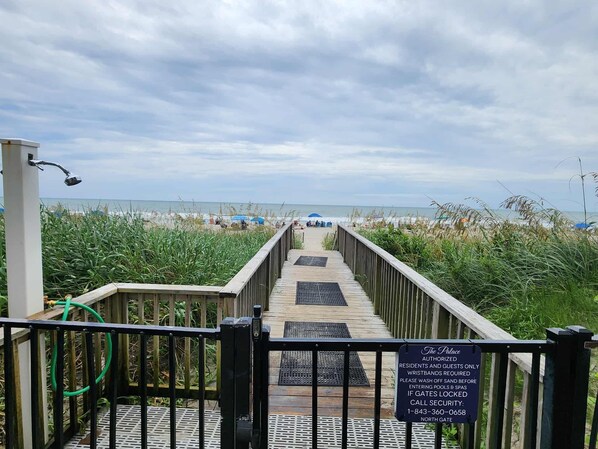 A wooden boardwalk leading to a beach with a sign indicating authorized access for residents and guests only, wristbands required, and a security contact number.