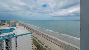 A coastal view with a beach, ocean, and buildings in the distance. - Coastal Luxe | Palace Twenty Oh Eight (Myrtle Beach)