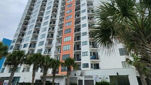 A high-rise building with multiple balconies, a swimming pool, and palm trees. - Coastal Luxe | Palace Twenty Oh Eight (Myrtle Beach)