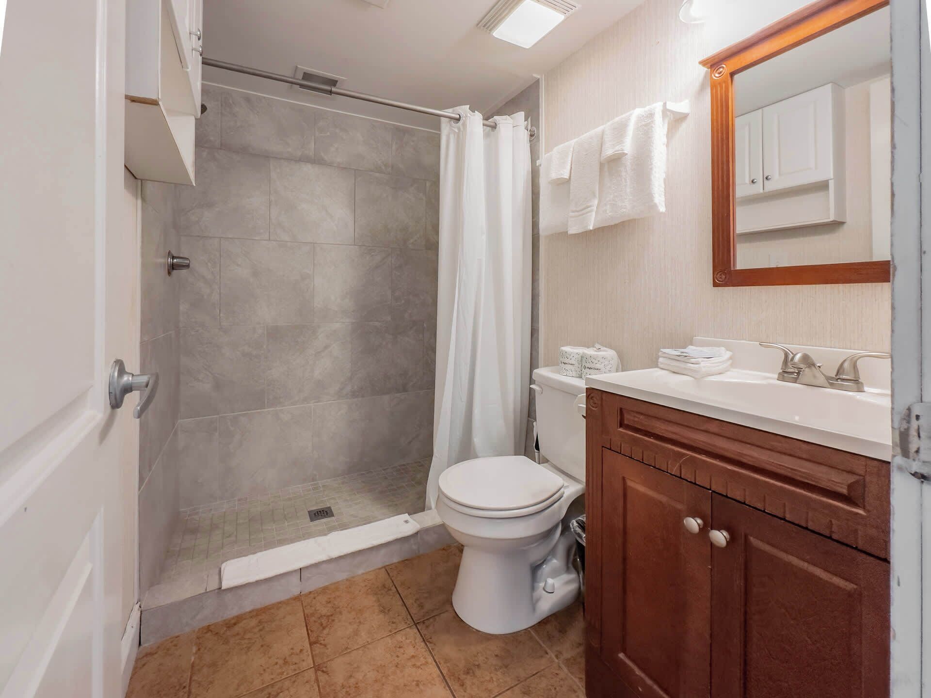 A bathroom with a shower, toilet, sink, and mirror.