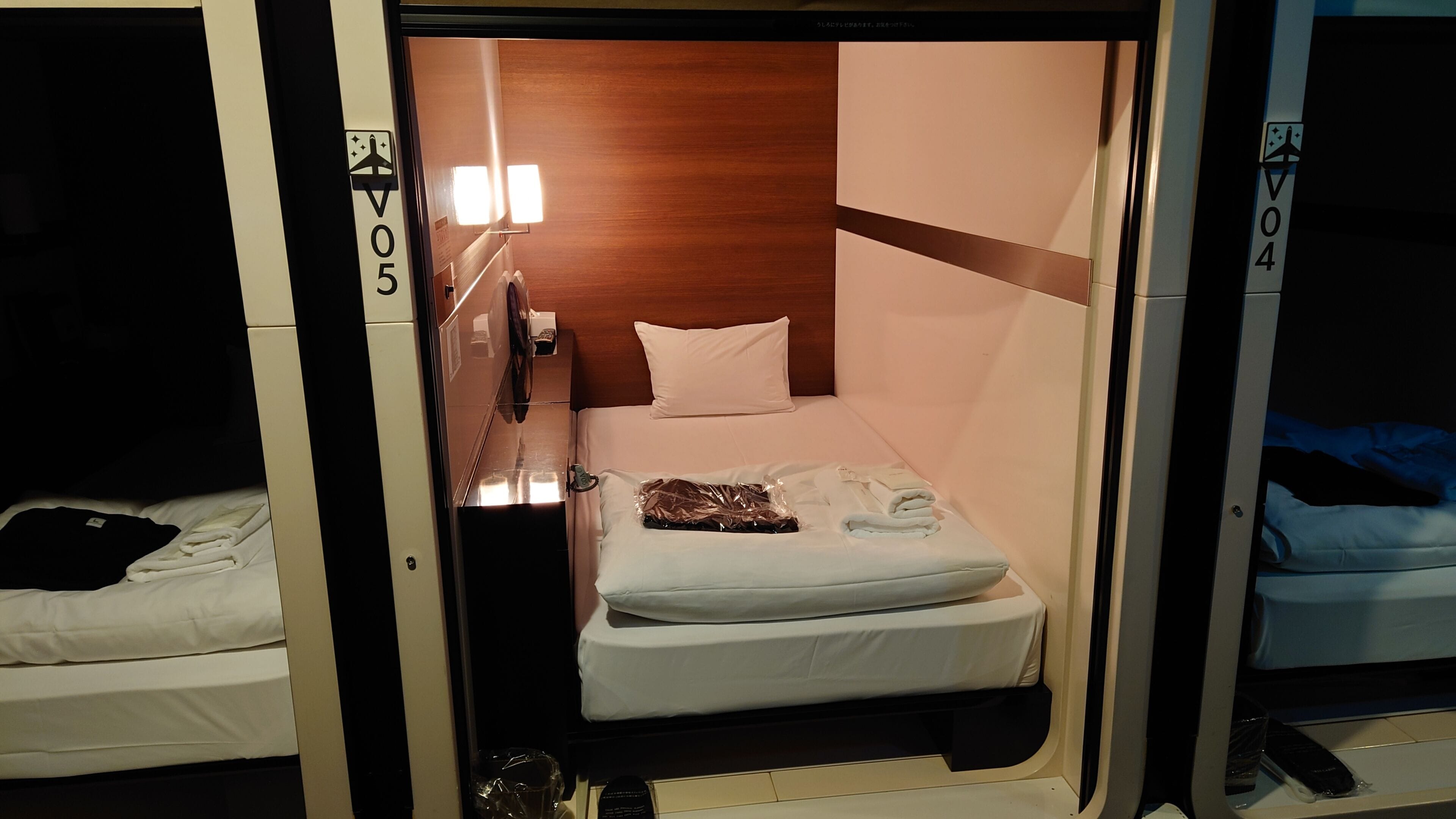 A compact room with a bed, a small table, and a wall-mounted light.
