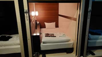 A compact room with a bed, a small table, and a wall-mounted light.