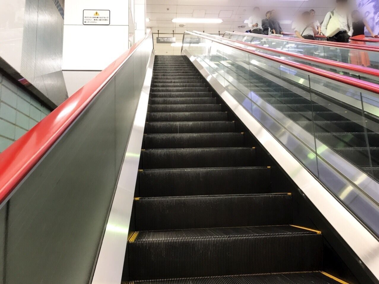 An escalator in a public indoor space with glass panels and metal railings.