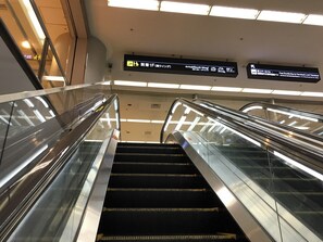 An indoor escalator with glass sides and overhead signs indicating directions to various terminals. - First Cabin Haneda Terminal 1 (Tokyo)