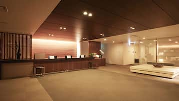 A modern reception area with a wooden reception desk, seating, and a glass partition.