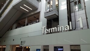 A modern building with a prominent 'Terminal 1' sign, multiple floors, and signs for 'Restaurants' and 'Shops'.