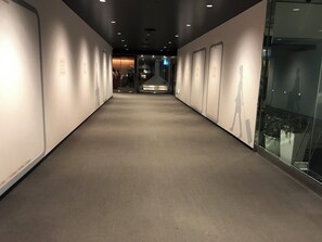 Un pasillo con piso de color claro, paredes blancas y paneles de vidrio a un lado.