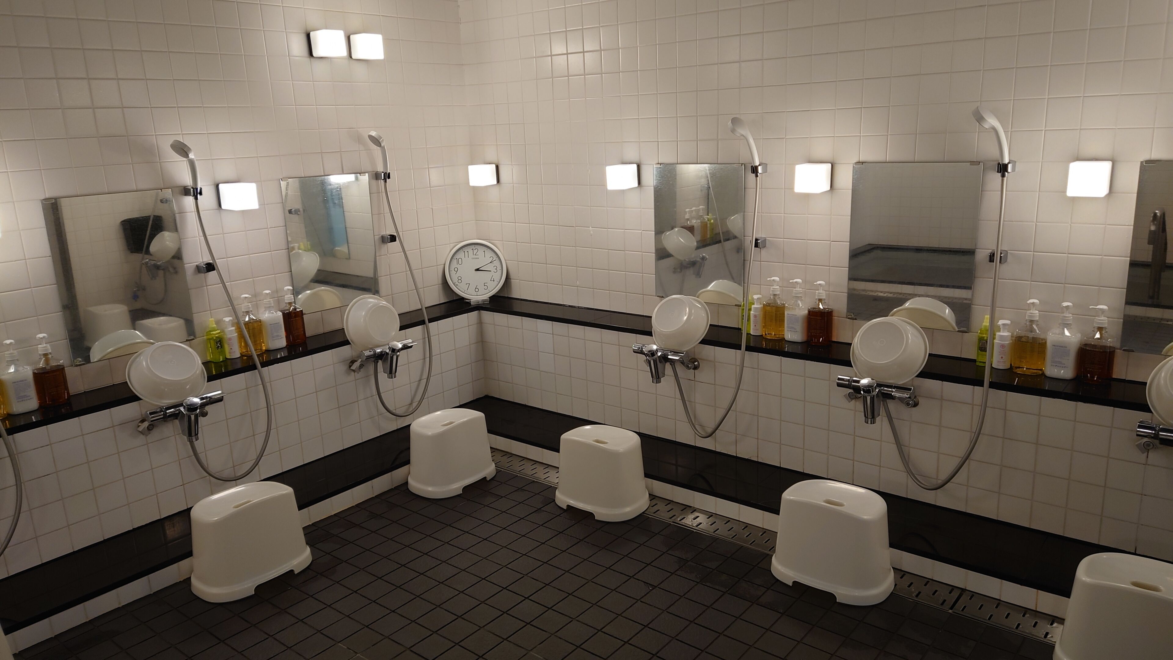 A public restroom with multiple urinals, hand dryers, and a clock on the wall.