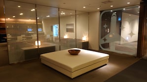 A modern interior with a glass partition, a white sofa, and a wooden bowl on a table. - First Cabin Haneda Terminal 1 (Tokyo)