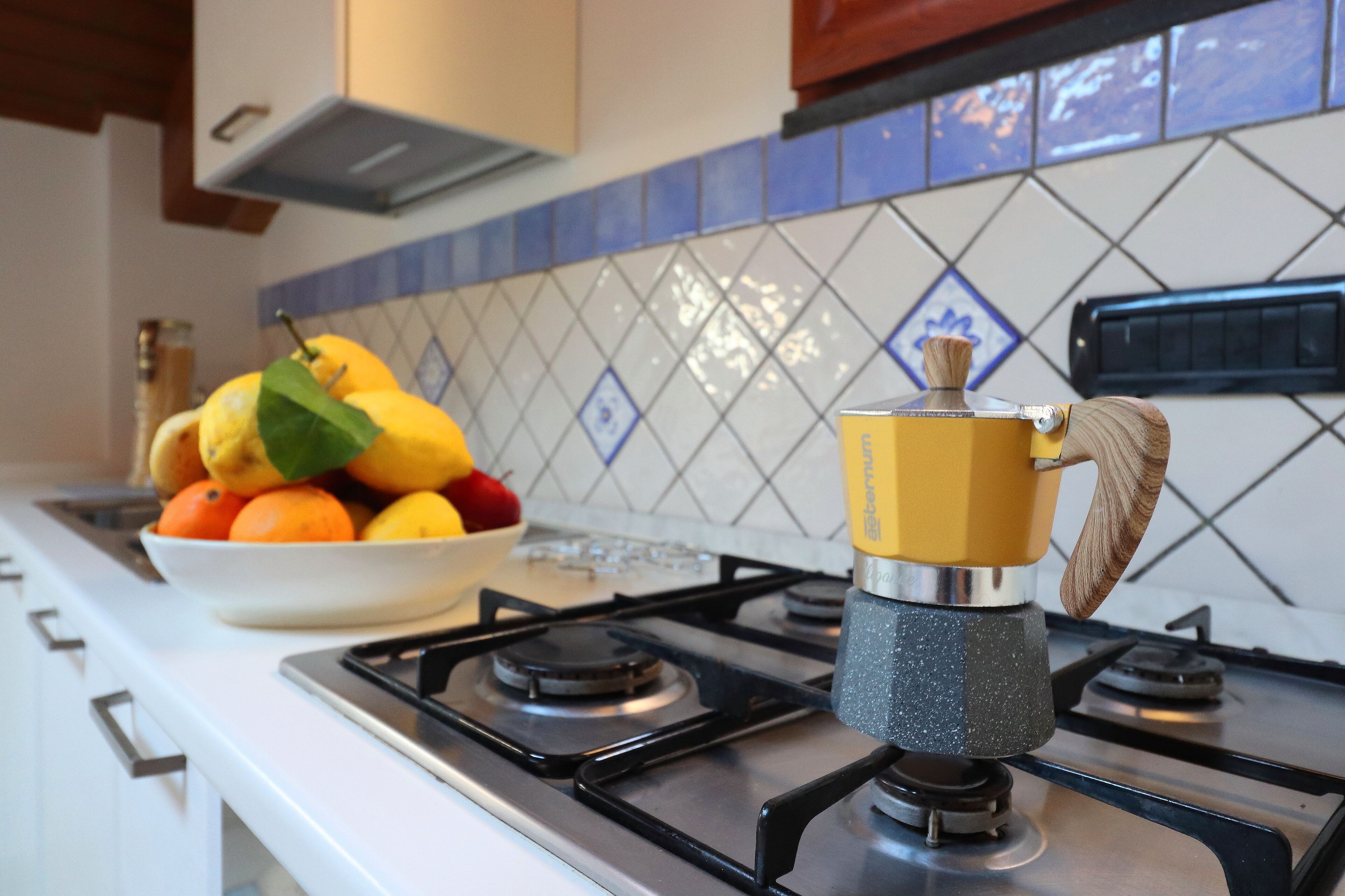 A kitchen with a gas stove, a bowl of fruit, and a spice rack.