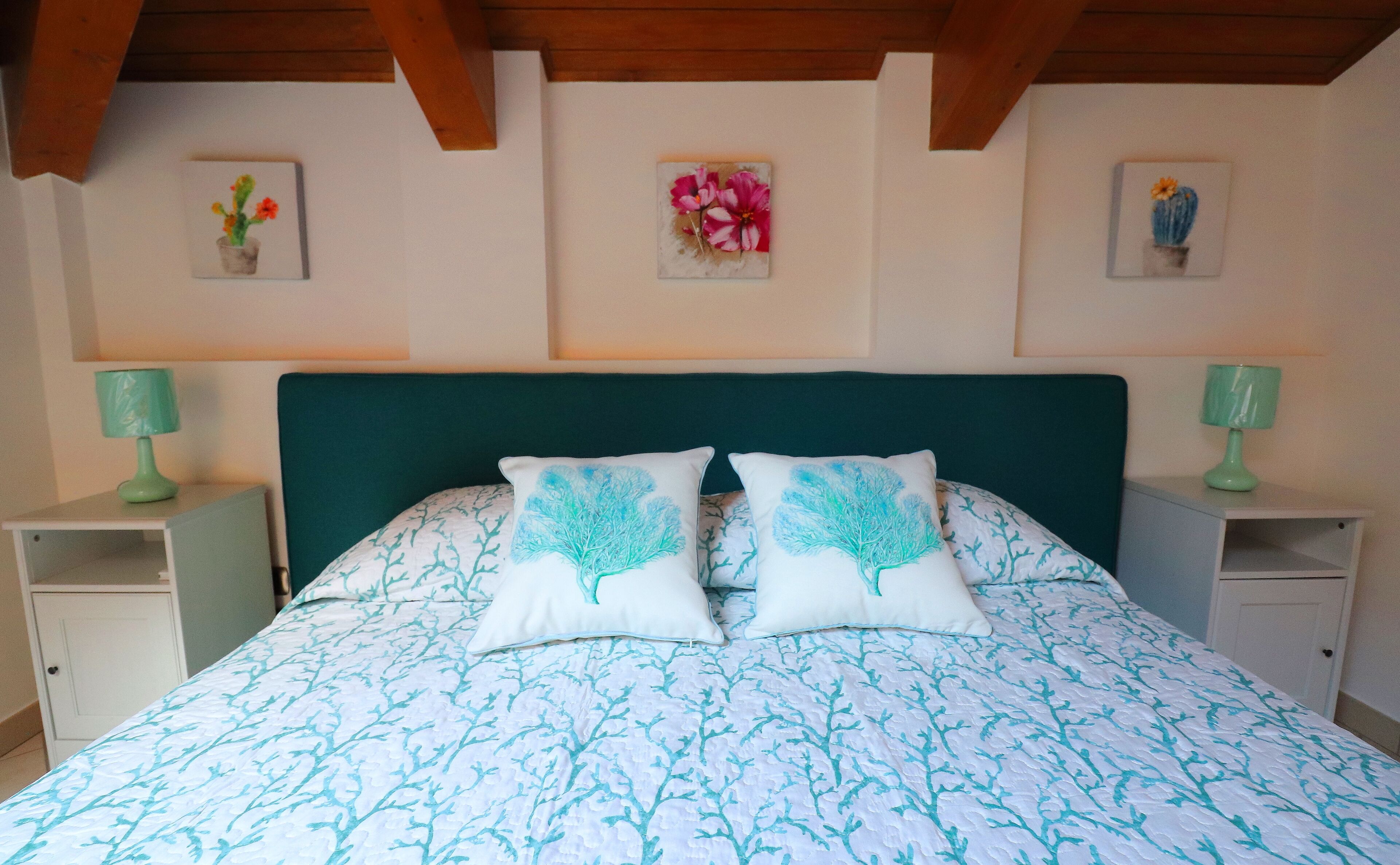 A bedroom with a green headboard, a floral-patterned bedspread, two matching pillows, and two bedside tables with green lamps.