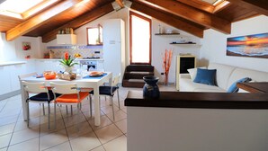 Una cocina moderna con armarios blancos, una mesa de comedor con sillas y vista al área de estar con un sofá y un cuadro.