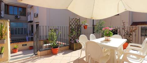 A patio with a table and chairs, surrounded by potted plants and a large umbrella.