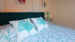 Un dormitorio con una cama, dos almohadas con diseños de árboles, una mesita de noche con una lámpara y una obra de arte en la pared.