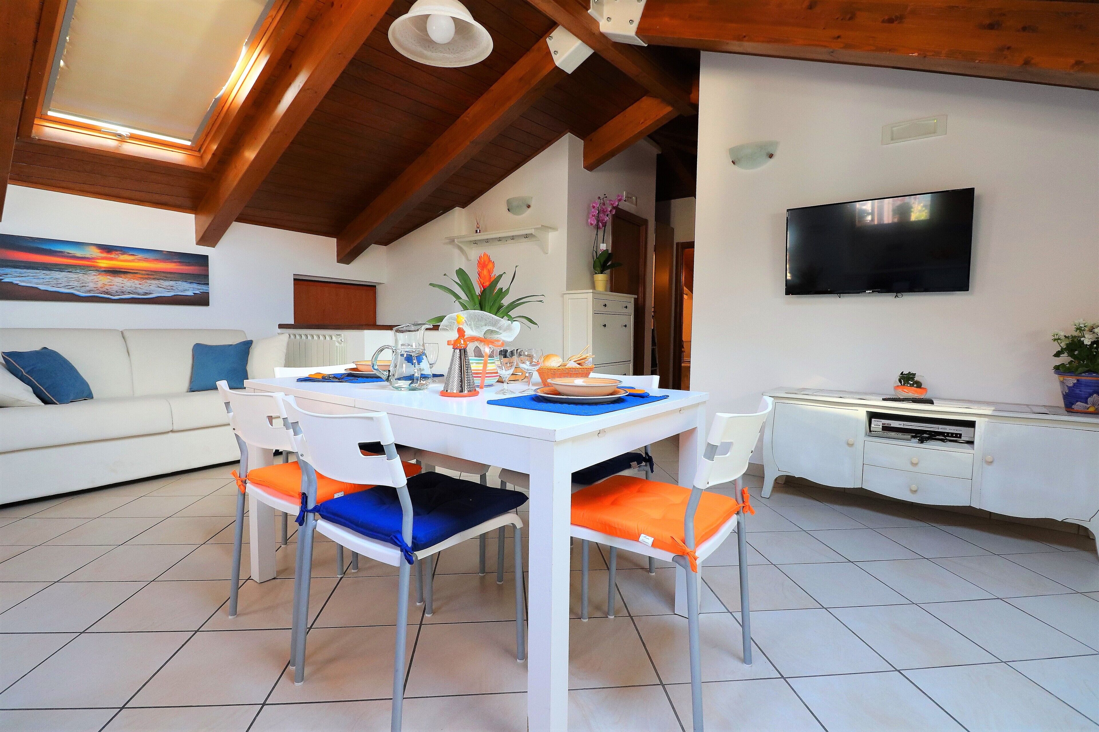 A dining area with a white table, four chairs, and a television on the wall.