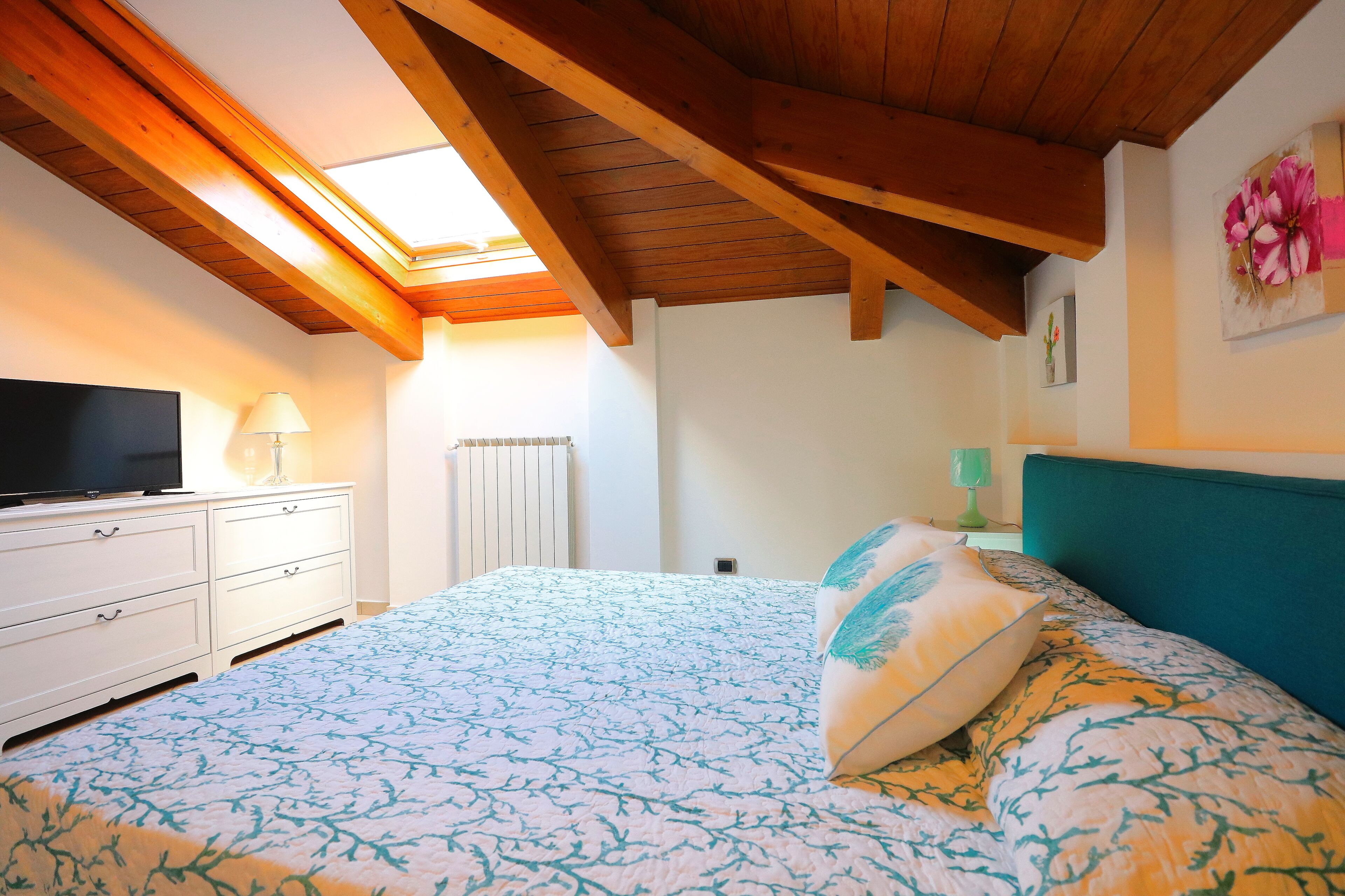 A bedroom with a bed, a TV, a dresser, and a skylight.
