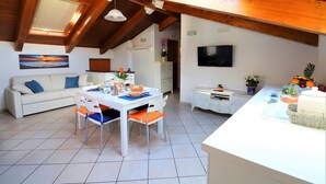 Una sala moderna con comedor, un sofá, un televisor y una cocina con televisor y plantas en macetas.
