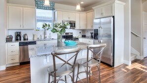 A modern kitchen with white cabinets, stainless steel appliances, a granite countertop, and a central island with bar stools. - Beautifully appointed home, ADA accessible and hot tub (Ocean Shores)