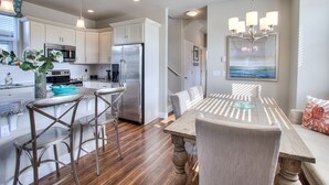 A modern kitchen with stainless steel appliances, a dining area with a wooden table and bar stools, and a chandelier. - Beautifully appointed home, ADA accessible and hot tub (Ocean Shores)