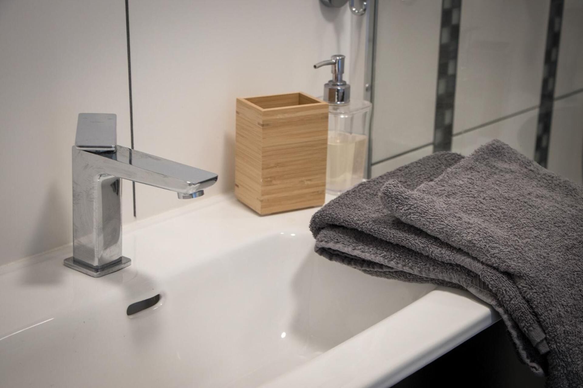 Un baño con un lavamanos blanco, una caja de madera y una botella de jabón.