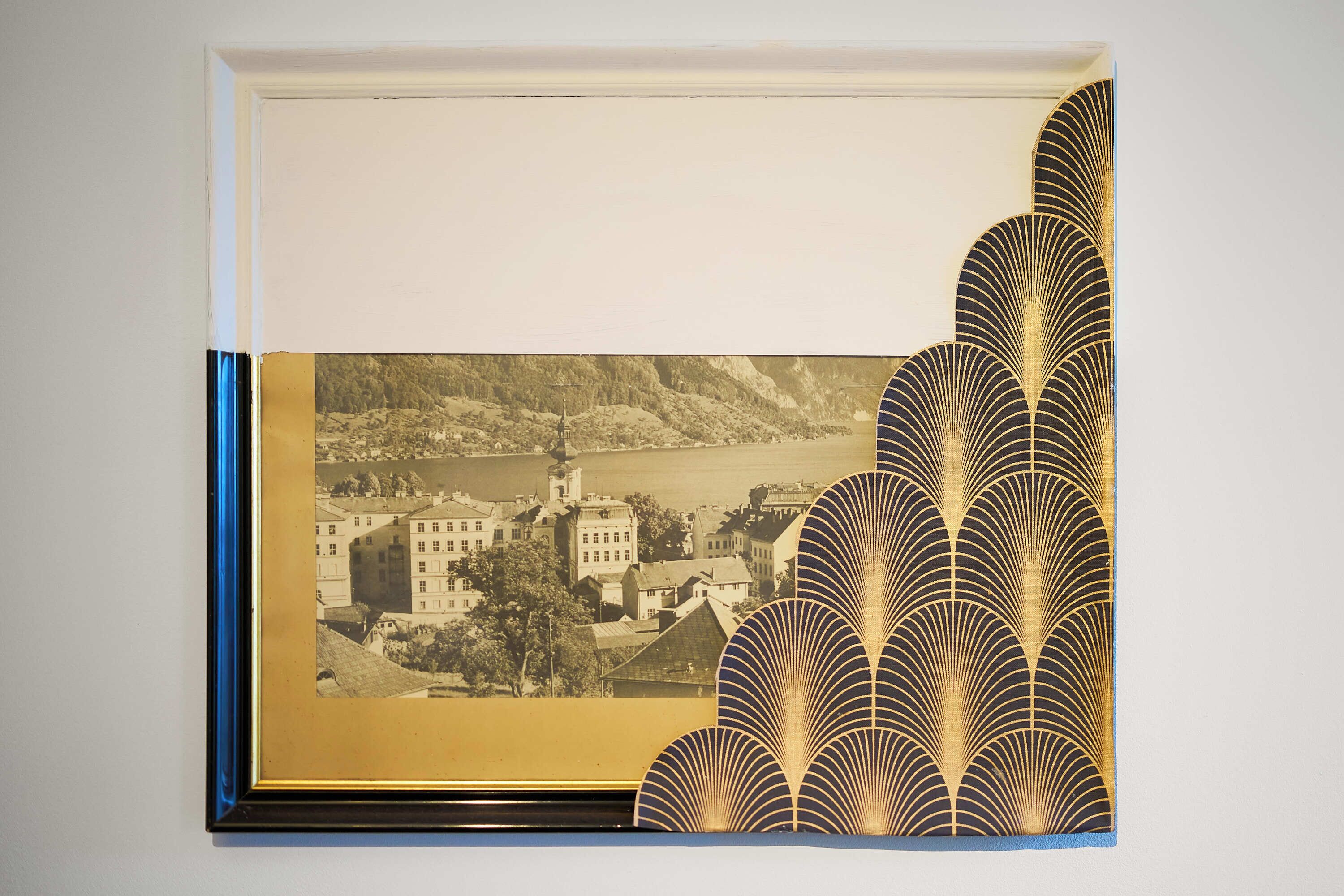 Fotografía enmarco de un pueblo con edificios y un río, rodeado de un diseño decorativo dorado y negro.