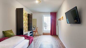 A modern hotel room with a bed, a desk, a chair, a flat-screen TV, and a large window with curtains.