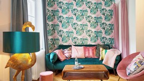 Una sala de estar con un sofá color esmeralda, un sillón rosa, una mesa de centro de madera y una lámpara de pie con base dorada.
