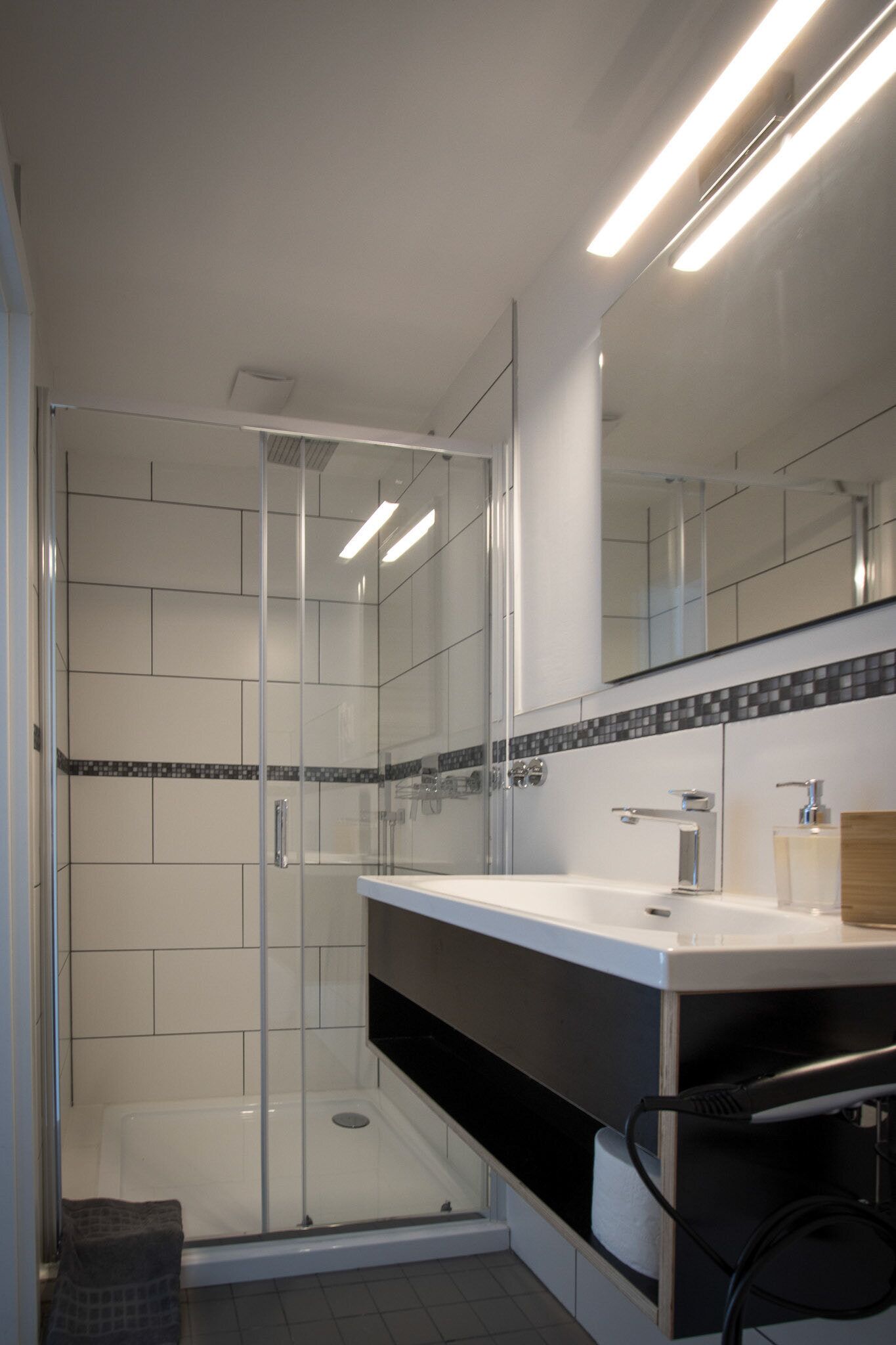 Un baño moderno con ducha acristalada, un lavabo blanco y encimera negra, y un espejo sobre el lavabo.