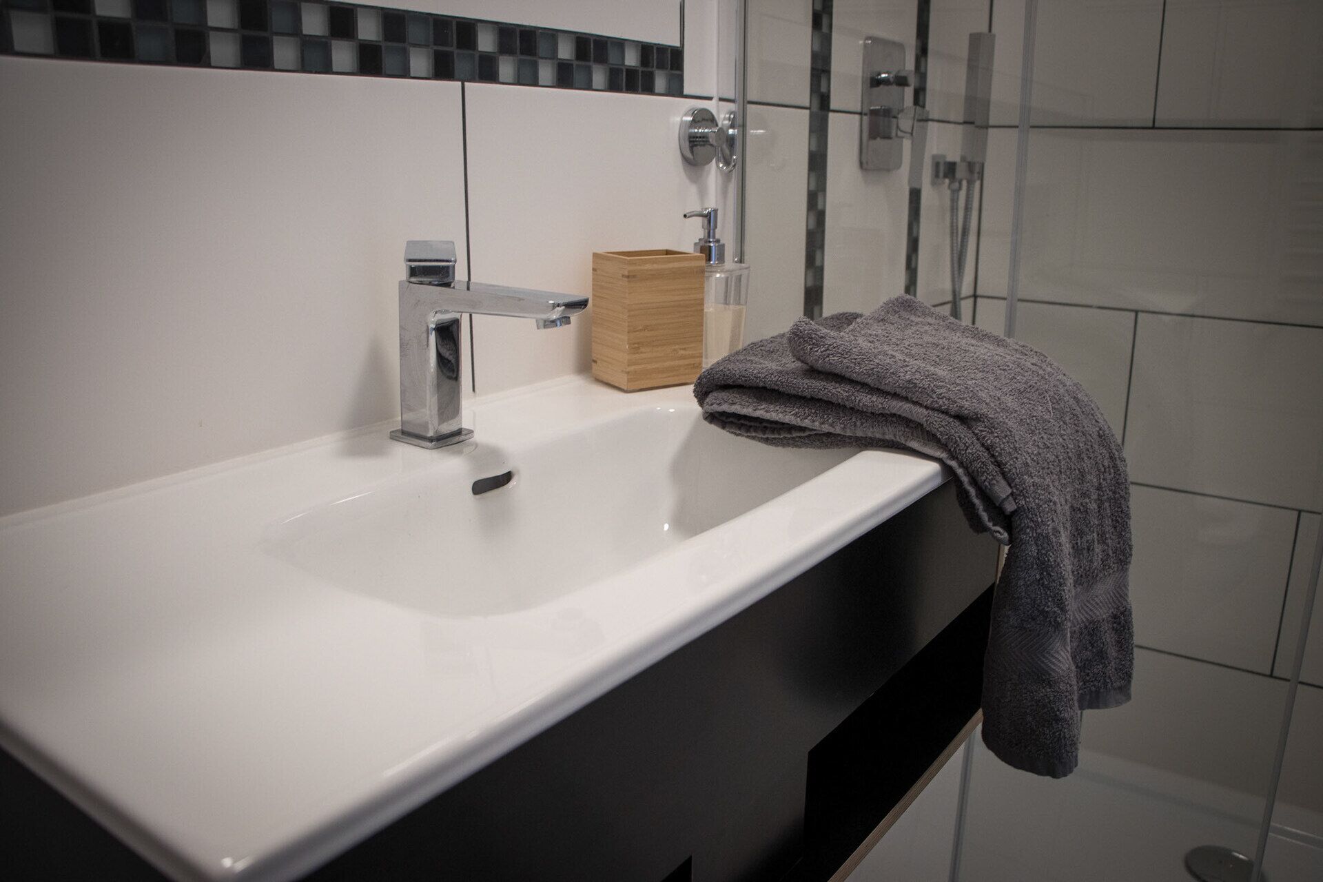 A bathroom with a white sink, a wooden soap dispenser, and a towel on the counter.
