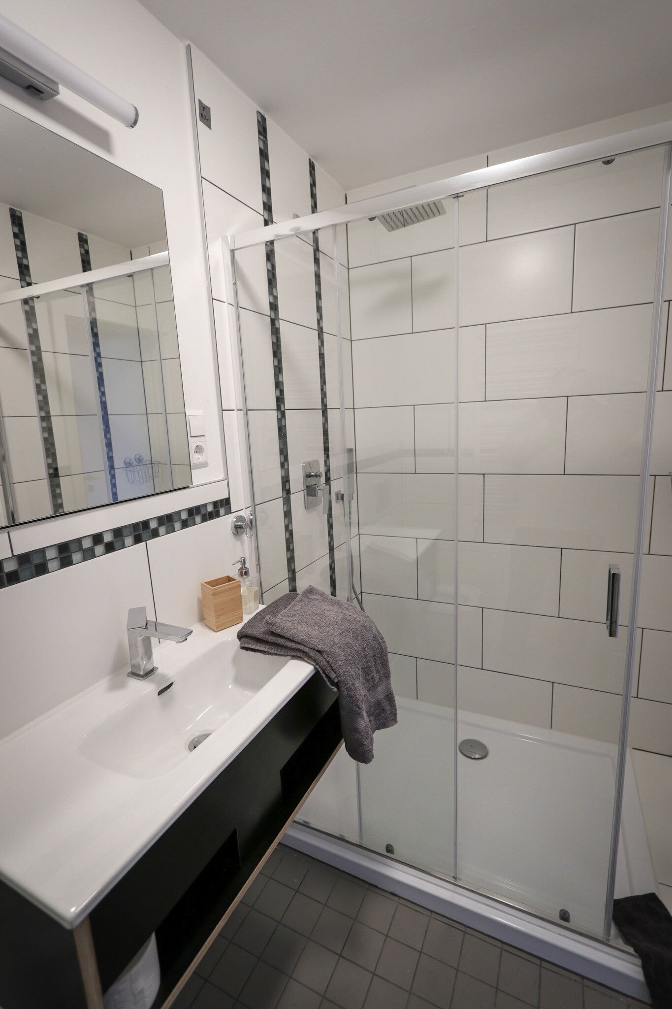A modern bathroom with a white sink, mirror, and glass shower enclosure.